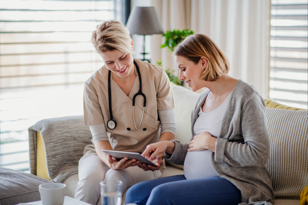 Nurse sitting on a couch helping a pregnant woman.